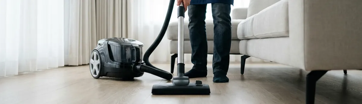 Professional house cleaner vacuuming a living room floor with a canister vacuum cleaner, Staten Island, NY.